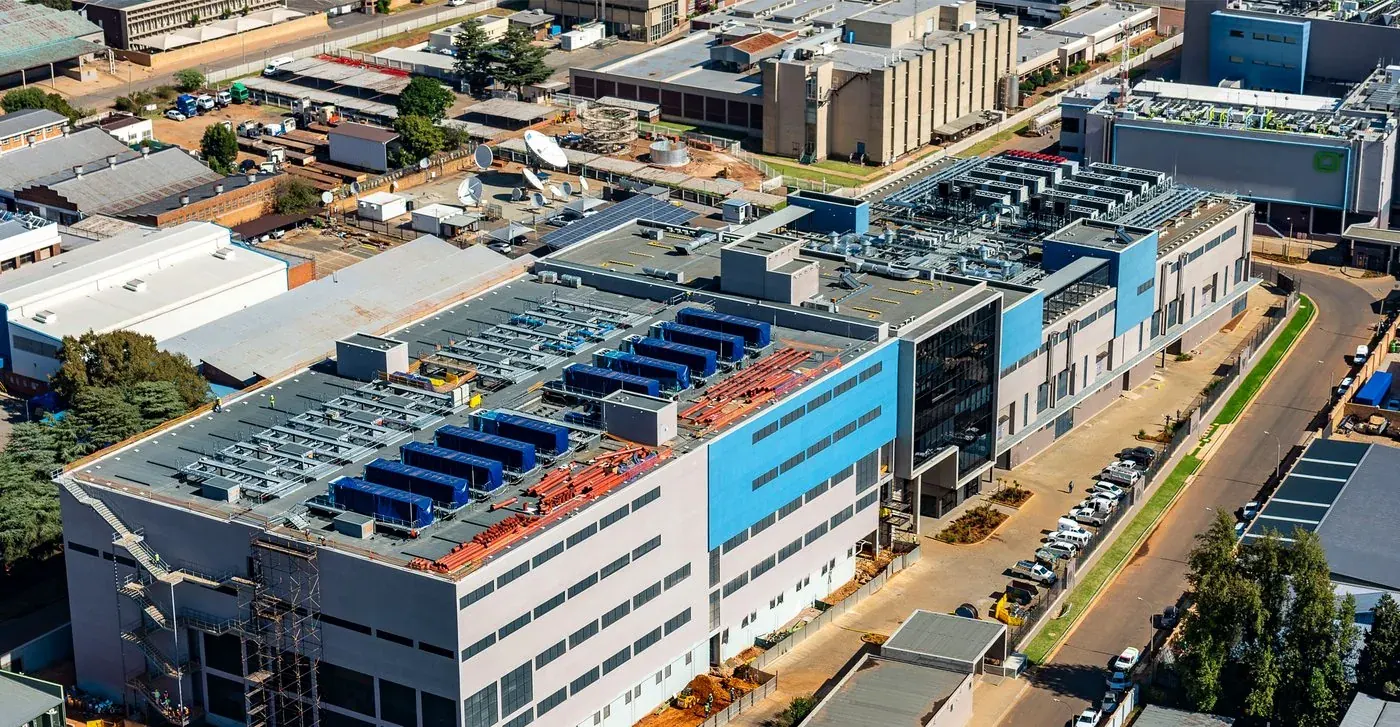 Aerial photograph of a data-centre campus showing rooftop cooling plant, a small solar array, construction in progress, and the surrounding industrial area
